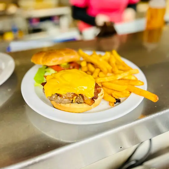 Bacon cheeseburger with melted cheese, lettuce and tomato next to a pile of fries on a white plate
