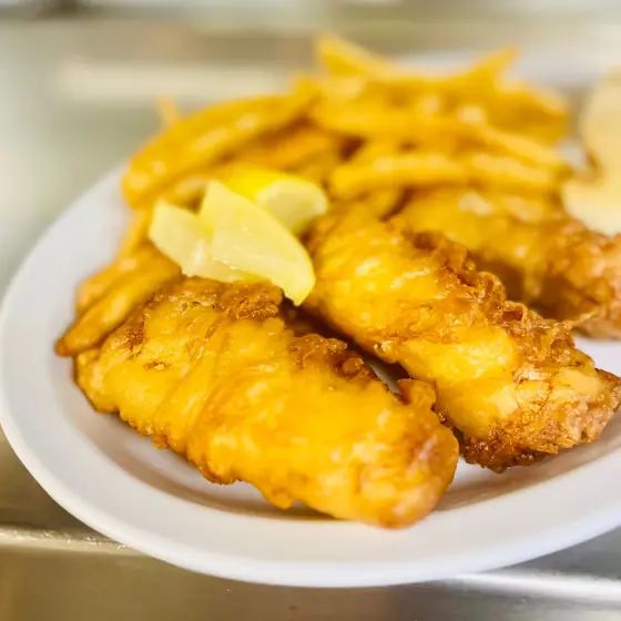 Beer-battered fish fillets and fries with lemon wedges on a white plate