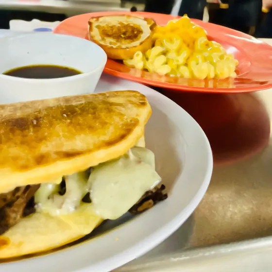 French dip sandwich with melted Swiss and a cup of au jus, mac and cheese on a plate behind