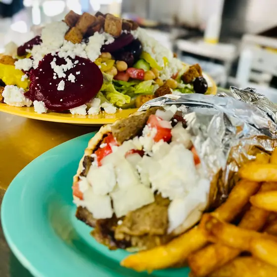Gyro wrapped in foil, topped with feta, tomato and onion, with fries, and a Greek salad with beets behind